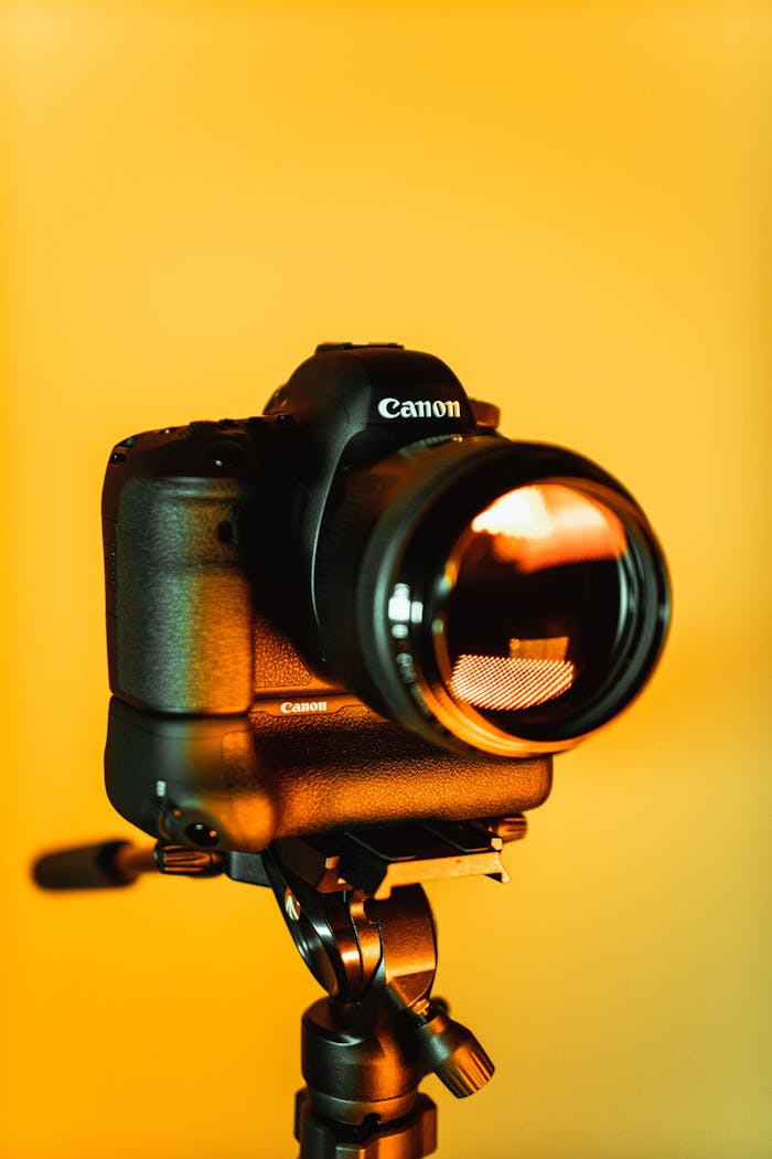 Close-up of a DSLR camera mounted on a tripod with an orange backdrop, highlighting photography equipment.